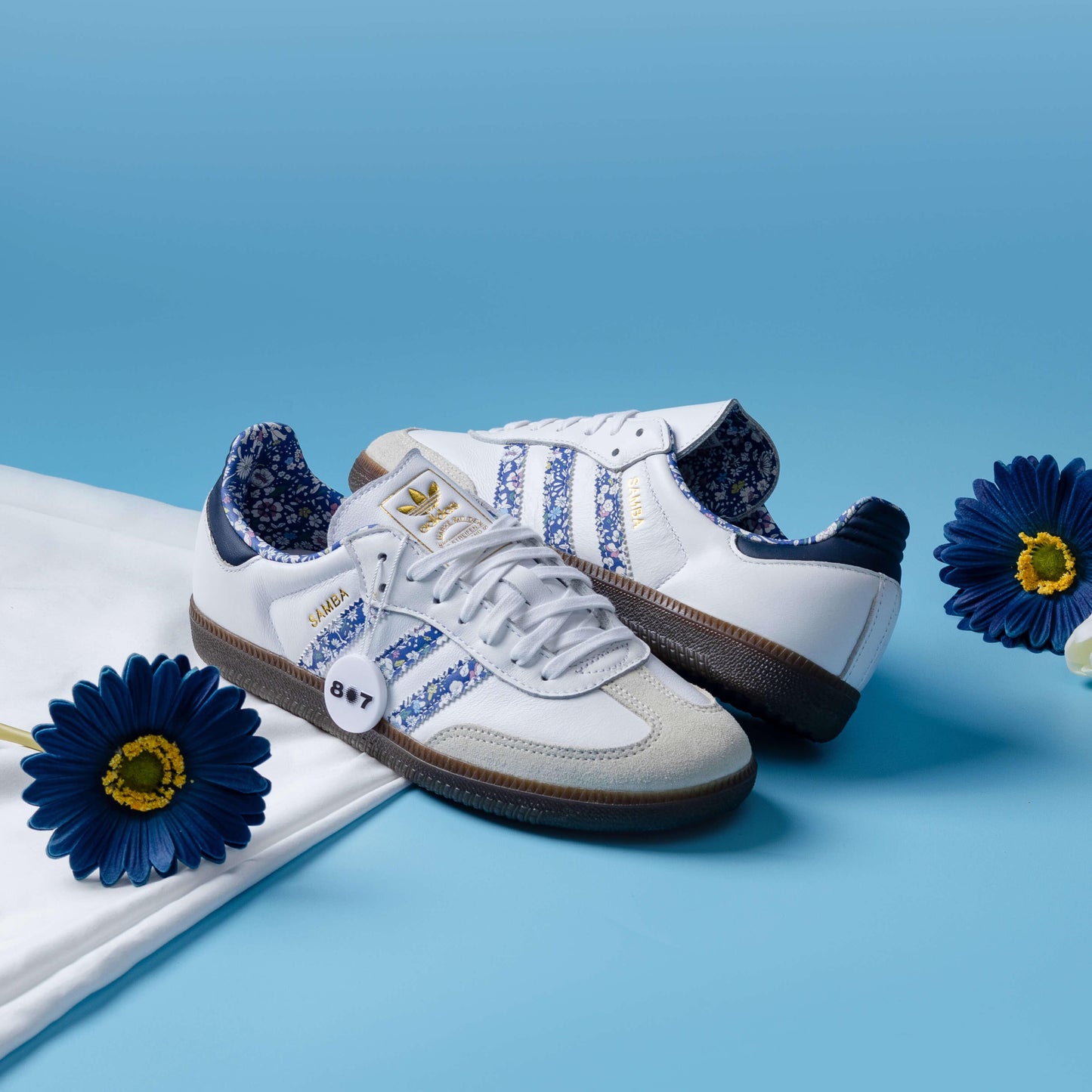 Adidas Samba Liberty LDN sneakers feature a white leather upper with blue floral-printed stripes.