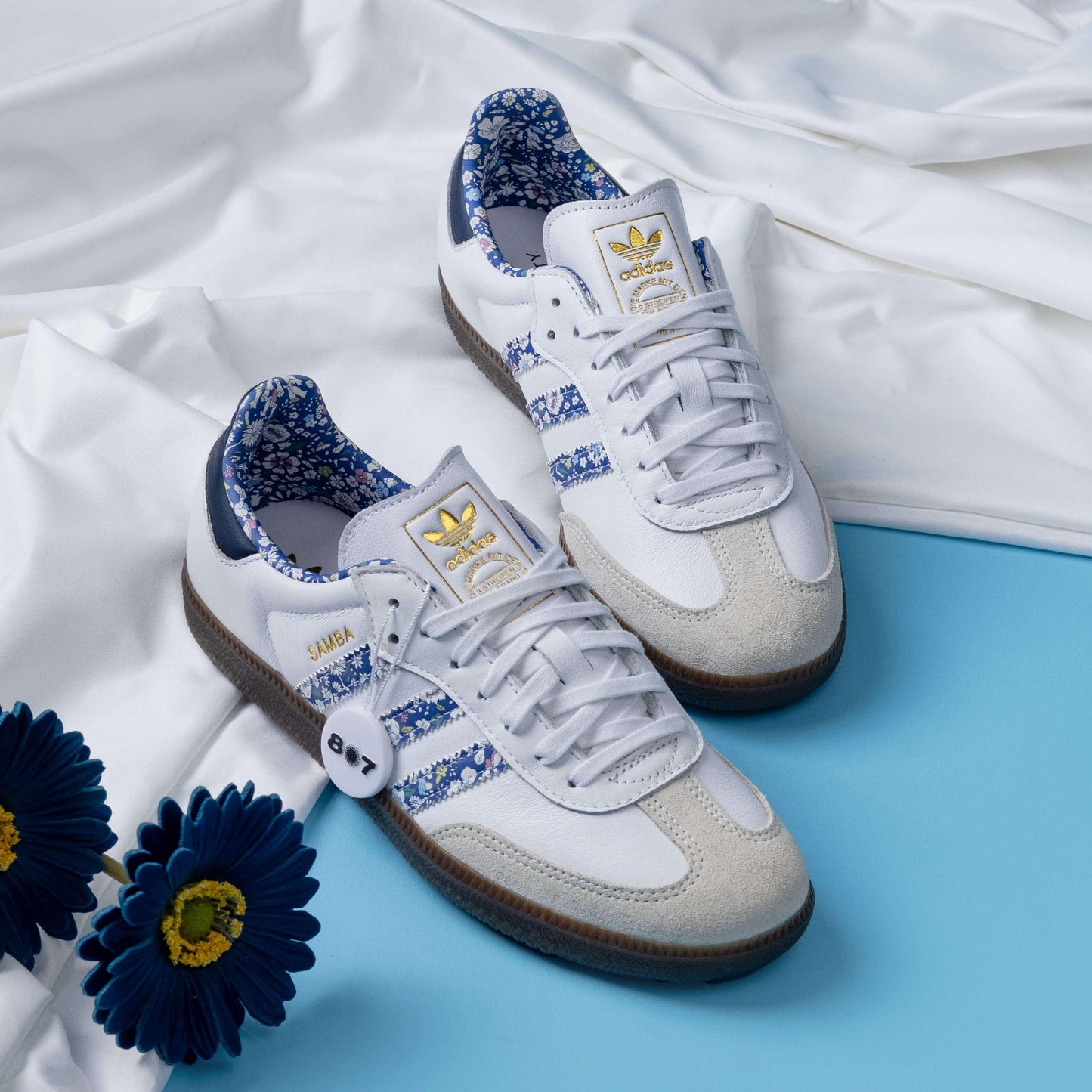 Adidas Samba Liberty LDN sneakers feature a white leather upper with blue floral-printed stripes.