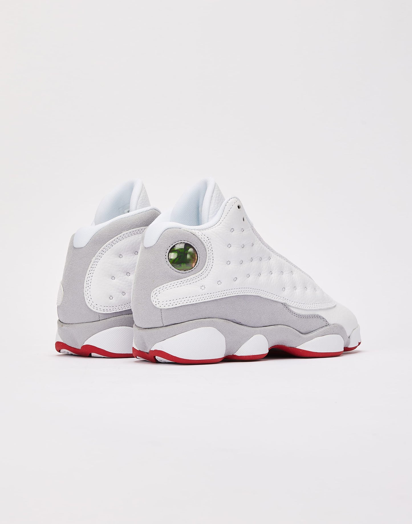 These are the Nike Air Jordan 13 Retro "Wolf Grey" sneakers, featuring a white tumbled leather upper with a signature green holographic eye on the heel.